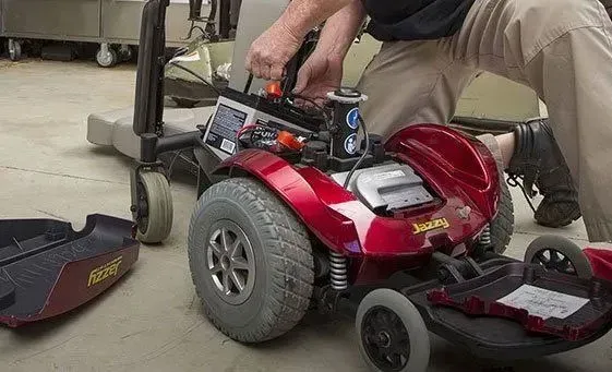 A man in brown slacks messing with wires inside of a mobility scooter