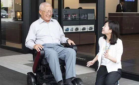 A woman examining an electric wheelchair while speaking to the man sitting in it