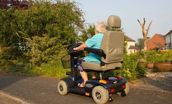 An elderly woman traveling down a neighborhood sidewalk in a mobility scooter