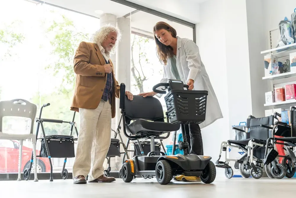 A woman in a lab coat showing an electric mobility chair to an older man
